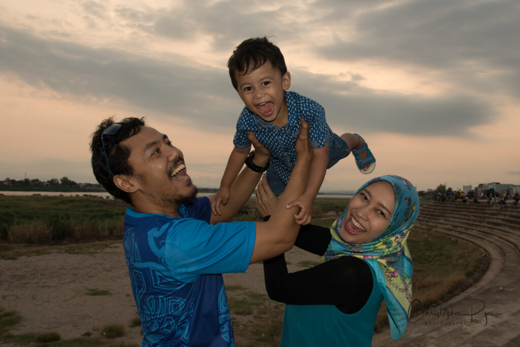 Muslim family holding their young son in the air while standing near the Mekong River in Laos.